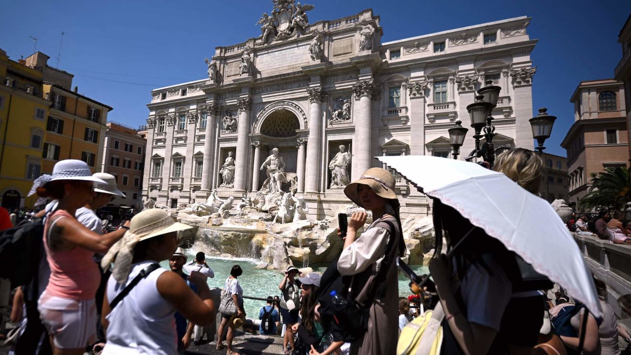 Tourist protect themselves with hats and umbrella at the Trevi Fountain during a heatwave in Rome on August 21 2023. (Photo by Filippo MONTEFORTE / AFP) (Photo by FILIPPO MONTEFORTE/AFP via Getty Images)